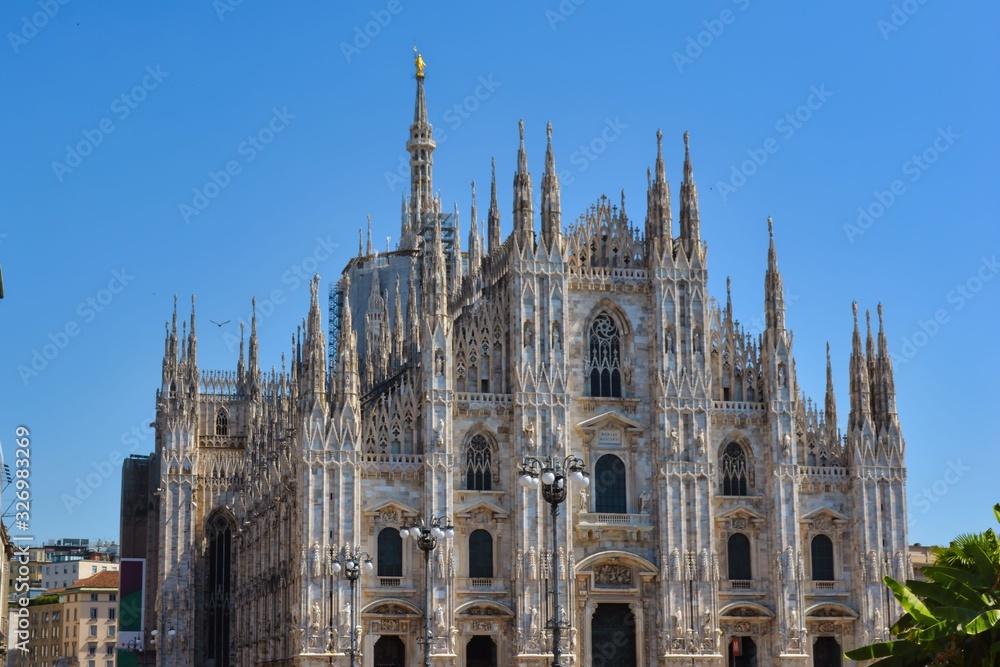 white towers of Milan Cathedral Duomo with golden statue against the blue sky