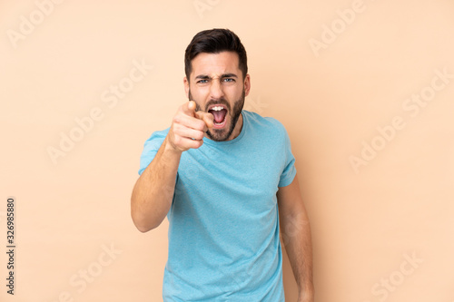 Caucasian handsome man isolated on beige background frustrated and pointing to the front