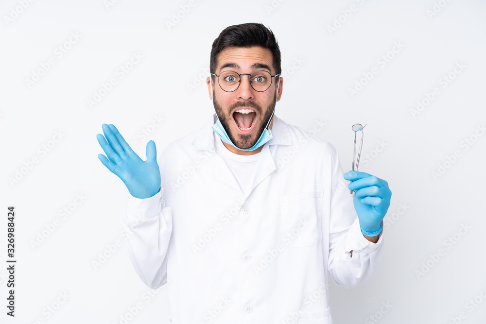 Dentist man holding tools isolated on white background with surprise facial expression Dentist man holding tools isolated on white background with surprise facial expression