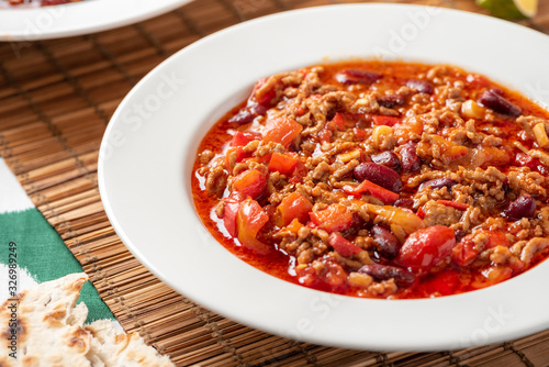 Chili con carne in a white bowl on a served table close-up. Chili con carne - a traditional Mexican soup with beans, tomatoes, minced meat and hot peppers. Mexican cuisine.