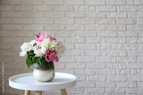 Empty apartment with minimal loft style interior, wooden floor and glass vase with bouquet of peonies on foreground and blank wall with a lot of copy space for text on background. Close up.
