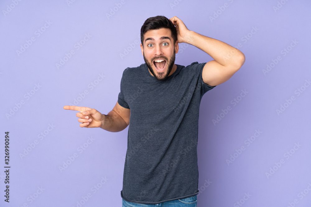 Caucasian handsome man surprised and pointing finger to the side over isolated purple background Caucasian handsome man surprised and pointing finger to the side over isolated purple background
