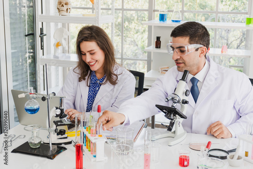 A male scientist doing experiments in a science laboratory while a female scientist happily typing the data on her laptop. Science experiment.