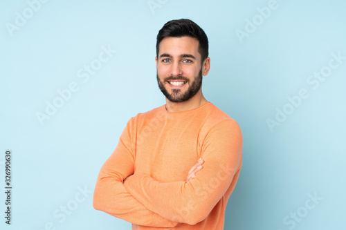 Caucasian handsome man with arms crossed and looking forward over isolated blue background