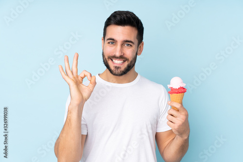 Caucasian man with a cornet ice cream isolated on blue background showing ok sign with fingers