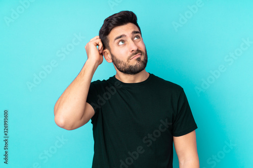 Quadro su tela Caucasian handsome man isolated on blue background having doubts and with confus