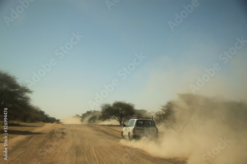 samochód terenowy mknący po szutrowej drodze afrykańskiej sawanny zostawiający za sobą chmurę kurzu © KOLA  STUDIO