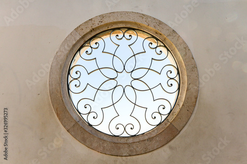 Round window with a black metal fence and a pattern in an old stone facade with a view to the sky