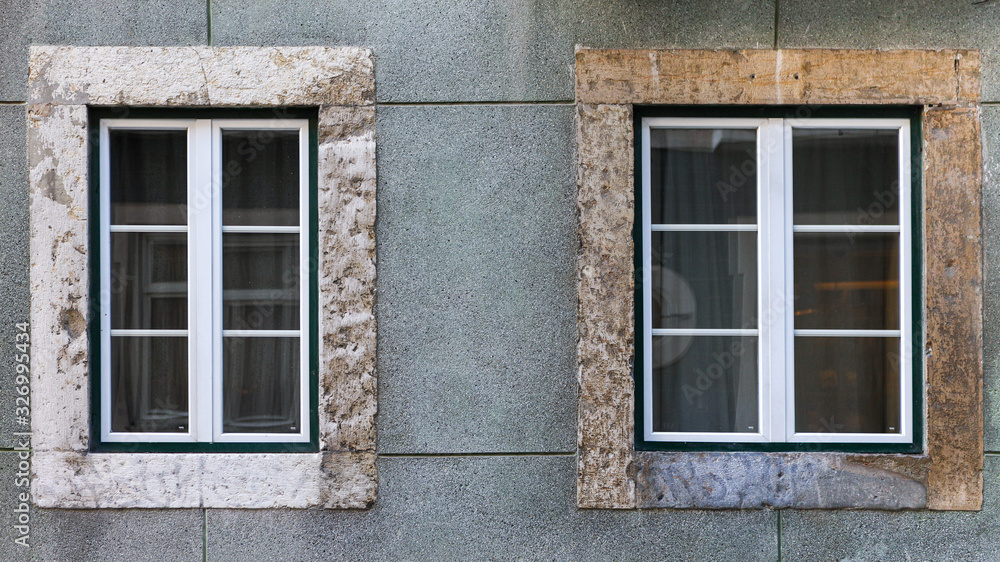 Two black windows inserted into a concrete exterior pale blue colored wall of a building. 