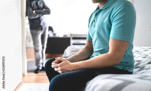 Gay couple in fight. Sad man in argument. Male friends or brothers in conflict. Stress or crisis in relationship. Infidelity and cheating or jealousy and mistrust. Upset guy sitting on bed at home.