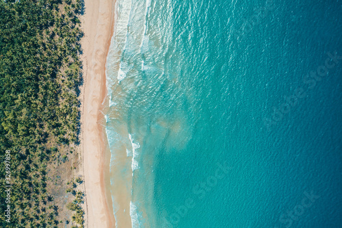 Aerial view to tropical sandy beach and blue ocean. Top view of ocean waves reaching shore on sunny day. Palawan, Philippines.