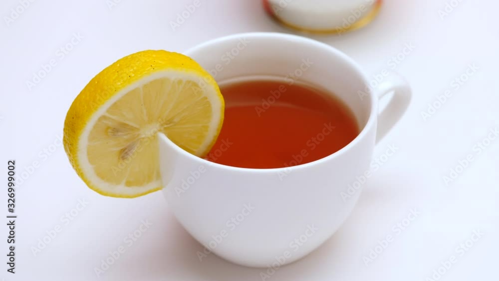 A serving of lemon tea in white porcelain cup. White table background. A serving of lemon tea in white porcelain cup. White table background.