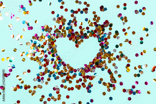 Heart shape made of golden colorful confetti splash on blue background. Festive backdrop of sparkles for birthday, valentine's day, carnival
