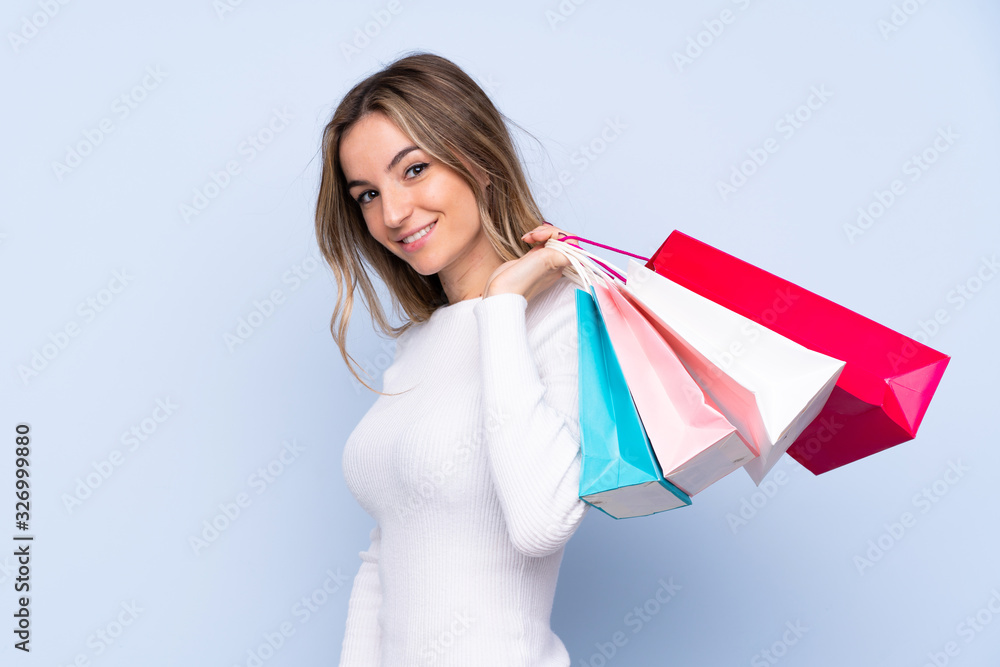 Young woman over isolated blue background holding shopping bags and smiling Young woman over isolated blue background holding shopping bags and smiling