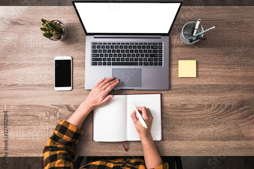 top view female hands using a laptop and writing in notebook. phone and sticky notes on table