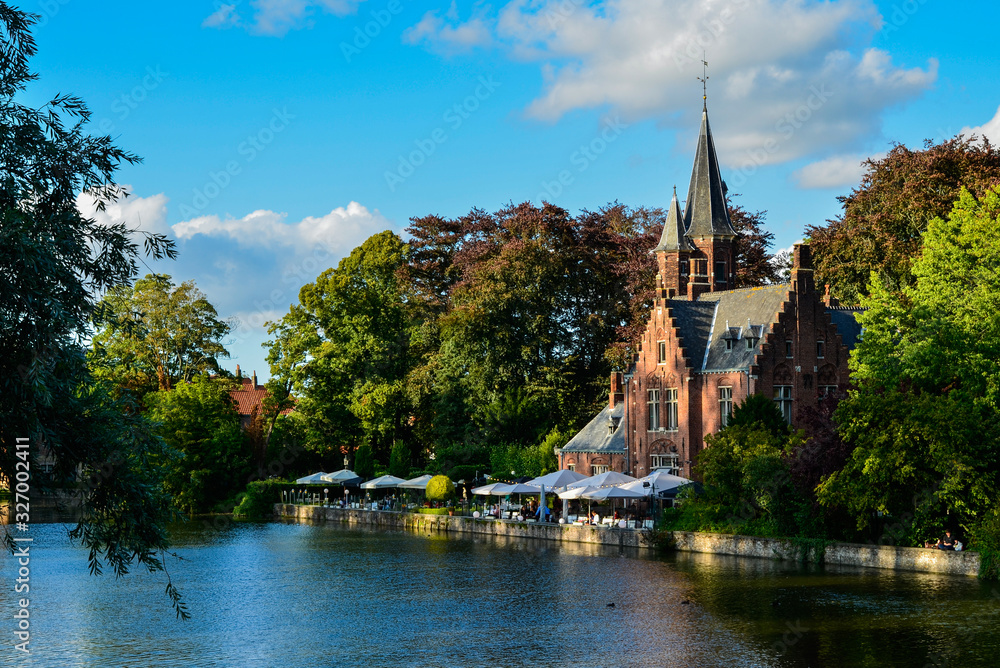 Bruges, Belgium. August 2019. The lake and minnewater park are the most romantic place. The body of water on which the red brick castle and the large trees with green foliage are reflected.