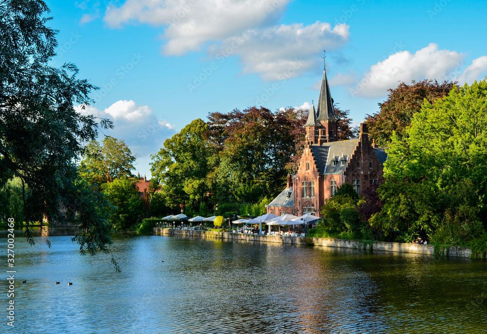 Bruges, Belgium. August 2019. The lake and minnewater park are the most romantic place. The body of water on which the red brick castle and the large trees with green foliage are reflected.