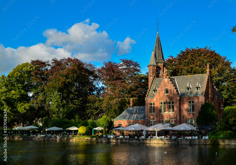 Bruges, Belgium. August 2019. The lake and minnewater park are the most romantic place. The body of water on which the red brick castle and the large trees with green foliage are reflected.