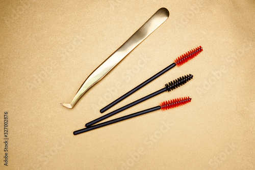  eyelash extension tools, golden tweezers and red-black brushes on a gold background