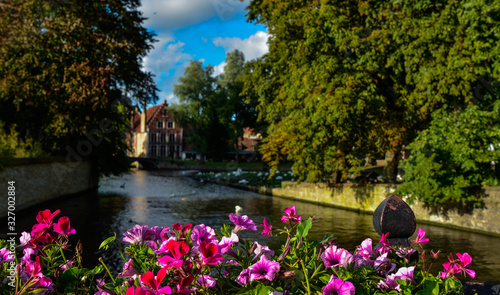 Bruges, Belgium. August 2019. View towards the historic center from the bridge with the Sashuis lock. A planter frames the canal that leads the gaze towards the city. Large green foliage on the sides. © Massimo Parisi