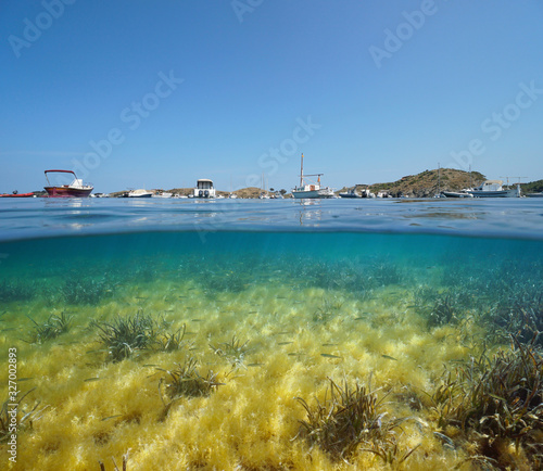 Spain Mediterranean sea, boats moored in Port Lligat bay and small fish with algae and seagrass underwater, split view over and under water surface, Costa Brava, Cap de Creus, Catalonia