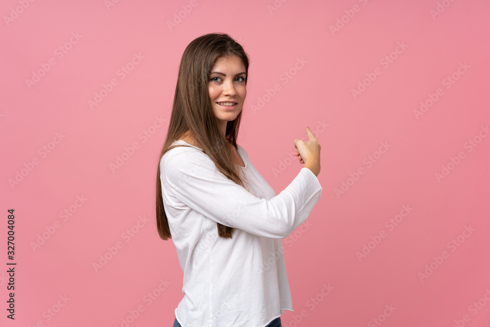 Young woman over isolated pink background pointing back Young woman over isolated pink background pointing back