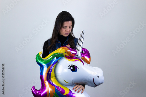 Portrait of attractive caucasian middle age womanunicorn balloon with closed eyes, keeps hands on chest, isolated on gray background studio shotblack sweater, denim jacket, jeans, dark air. Place for photo