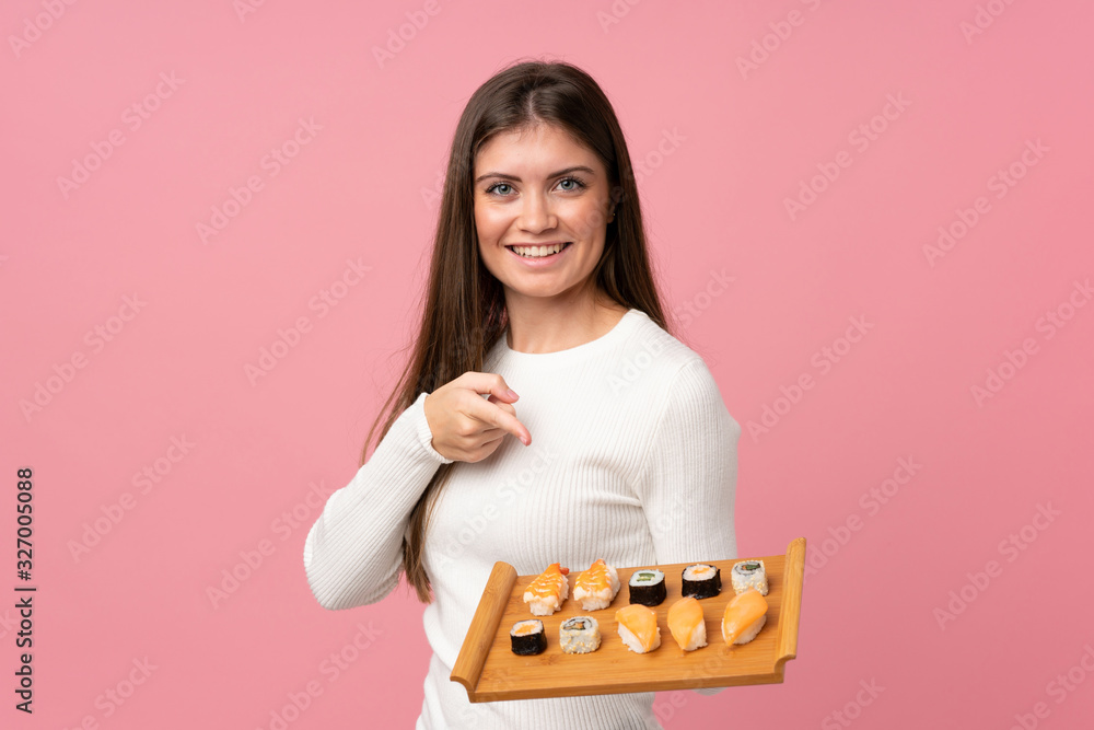 Young girl with sushi over isolated pink background and pointing it Young girl with sushi over isolated pink background and pointing it