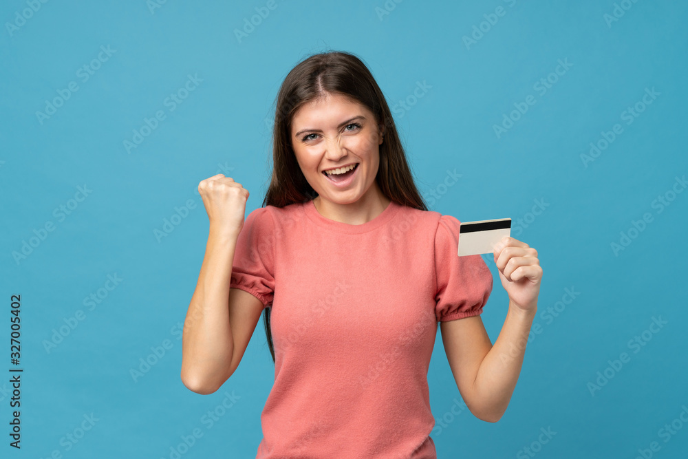 Young woman over isolated blue background holding a credit card Young woman over isolated blue background holding a credit card