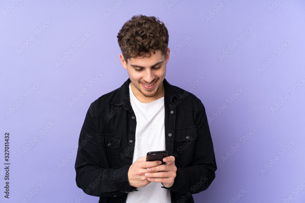 Caucasian man isolated on purple background sending a message with the mobile Caucasian man isolated on purple background sending a message with the mobile