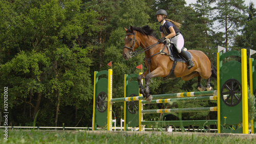 Young female jumping over oxer fence on strong brown horse