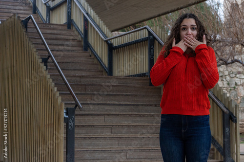 shocked scared attractive caucasian young woman model covering mouth with both hands, horrified stunned looking at camera isolated, in the park, orange sweater and jeans, long curly hair. Place for yo © Sergio Barceló