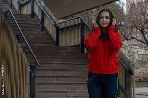 Portrait of beautiful young woman model listening music with headphones, in the park, orange sweater and jeans, long curly hair. Place for your text in copy space. © Sergio Barceló