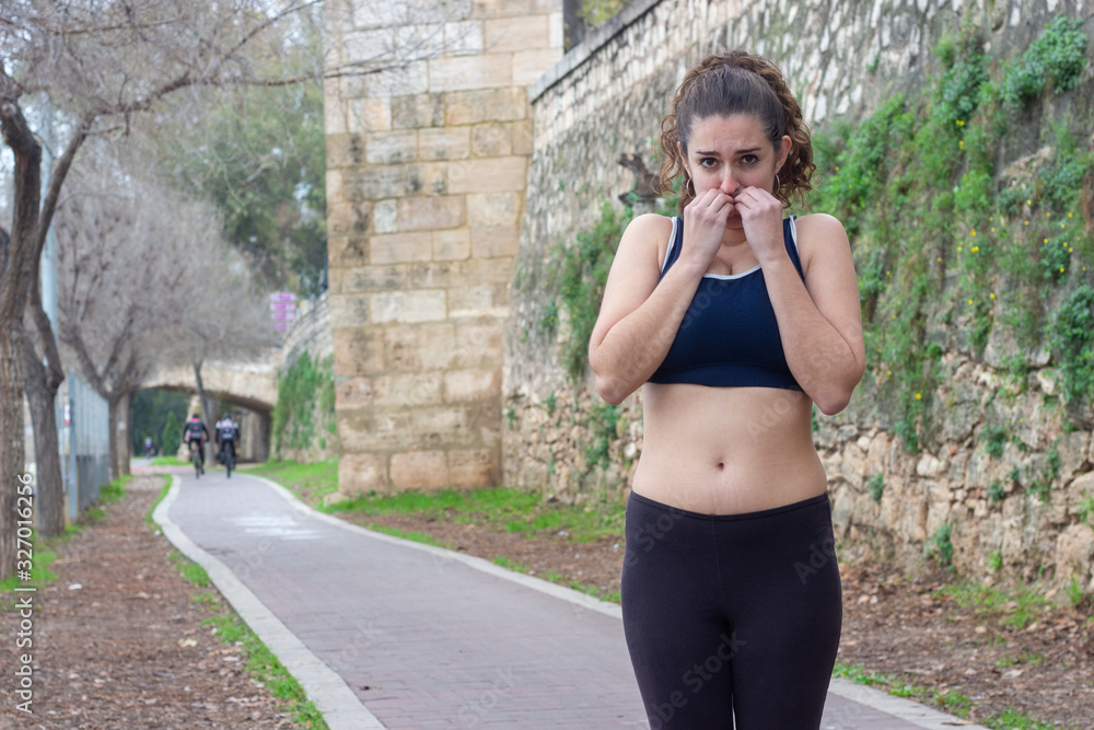 Portrait of scared athlete, caucasian young woman feels fear, bits nails, in the park, black top and black tights, long curly hair. Place for your text in copy space.