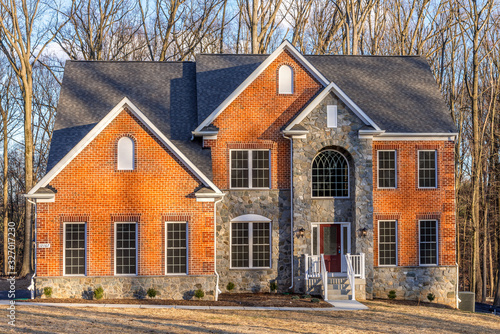 Luxury single family home with orange brick siding reinforced with decorative dressed Quoin brick, double hung sash windows,  semi circular gable windows and architectural stone cladding real estate photo