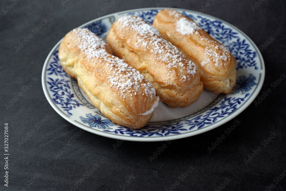 Eclairs with cream and powdered sugar on a plate Eclairs with cream and powdered sugar on a plate