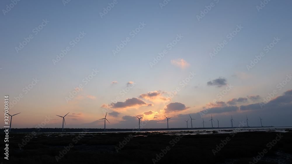 Sun setting in the evening, with silhouette of wind turbines in the far horizon.