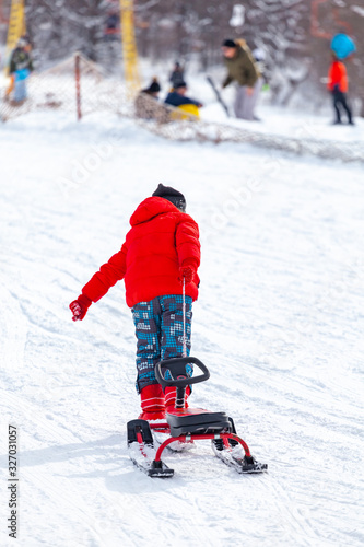 Back view of child in pulling sledge and running up snowy slope