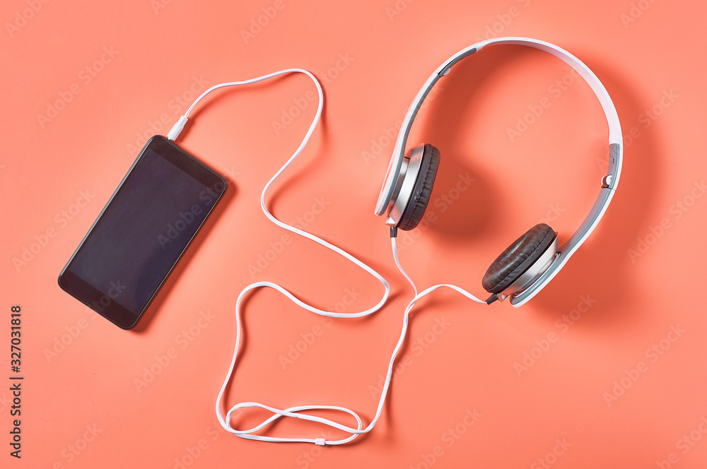 Modern white headphones with cable near smartphone or tablet on orange background. Call center concept. Top view Modern white headphones with cable near smartphone or tablet on orange background. Call center concept. Top view