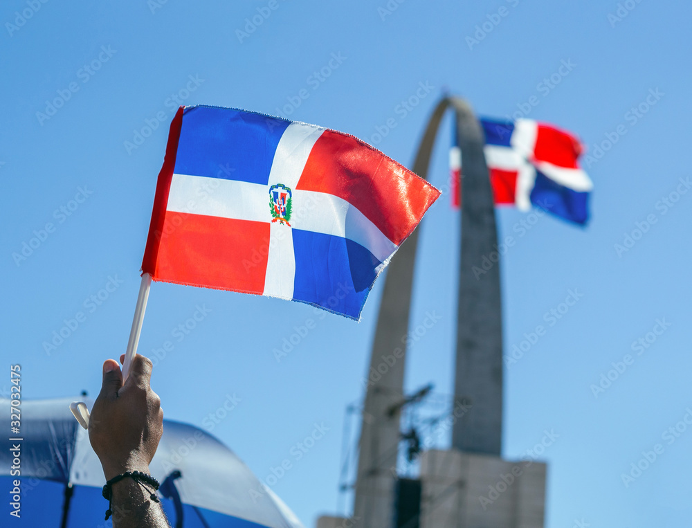 A hand holding the Dominican flag with the monument in the background - obrazy, fototapety, plakaty 