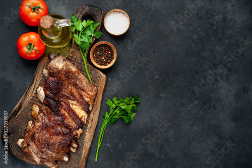 pork ribs with spices, tomatoes and herbs on a stone background with copy space for your text