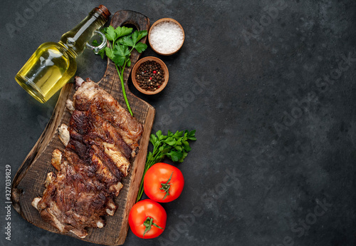 pork ribs with spices, tomatoes and herbs on a stone background with copy space for your text