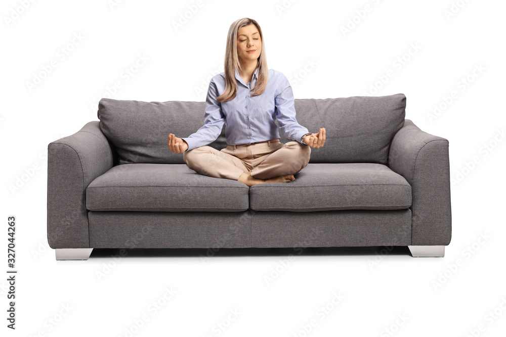 Young woman in formal clothes sitting on a sofa with crossed legs in a meditation pose Young woman in formal clothes sitting on a sofa with crossed legs in a meditation pose