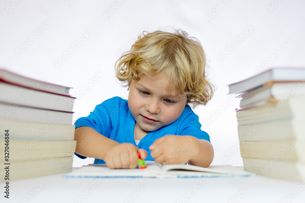 Little happy boy between 4 and 5 years old sitting at a desk doing his homework, with textbooks on his table Little happy boy between 4 and 5 years old sitting at a desk doing his homework, with textbooks on his table