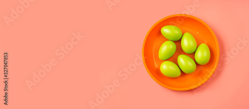 Top view of bright green Easter eggs in orange plate on vivid scarlet background