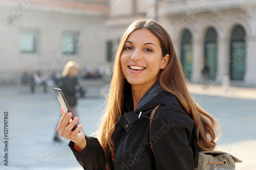 Portrait of beautiful brazilian student girl holding smart phone and looks at camera