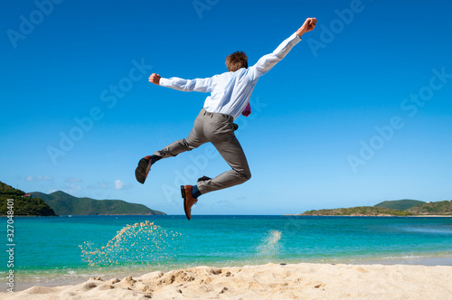 Businessman jumping into the air above a tropical beach clicking his heels together in celebration