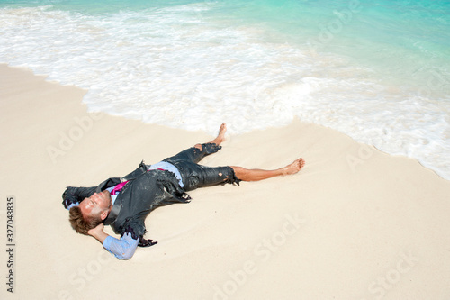Castaway survivor businessman washed up on a tropical beach relaxing in a ragged torn suit