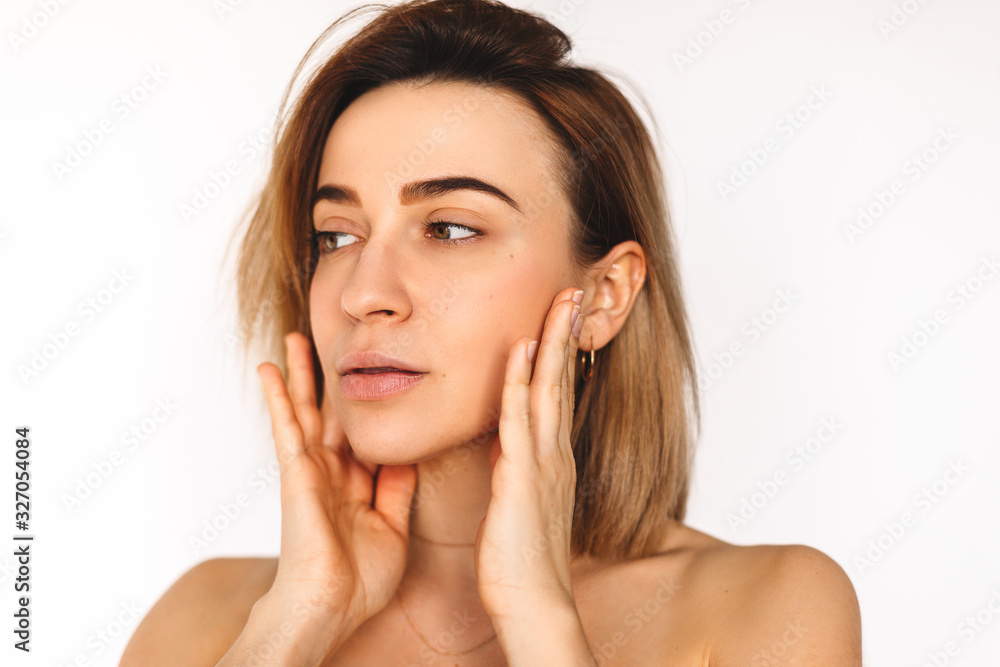 Beautiful woman face close up studio on white background. Sexy beautiful girl holding her cheeks looking to the side. Pretty woman clean fresh skin. Expressive facial expressions. Perfect fresh skin.