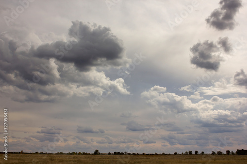 huge cumulus rain clouds and clouds in the sky in the sunshine above the field